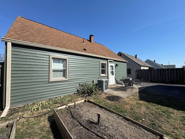 rear view of property with a patio, cooling unit, fence, roof with shingles, and a garden