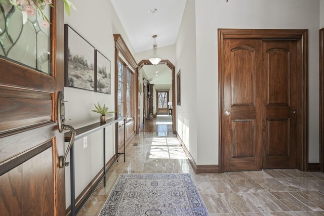 hall featuring baseboards, arched walkways, and marble finish floor