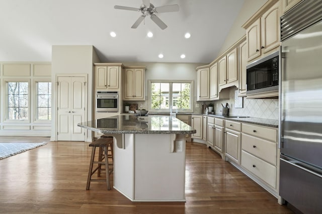 kitchen with lofted ceiling, black appliances, cream cabinetry, a kitchen bar, and backsplash