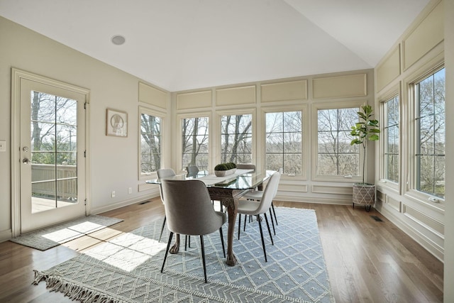 dining area with visible vents, lofted ceiling, wood finished floors, and a decorative wall