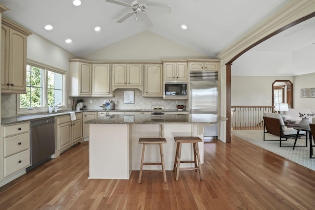 kitchen with dark stone countertops, a kitchen island, built in appliances, a kitchen bar, and cream cabinets