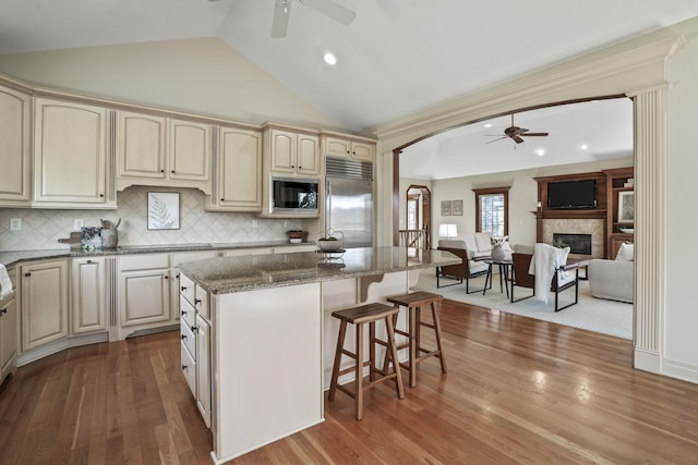 kitchen featuring a breakfast bar, ceiling fan, built in appliances, cream cabinets, and a center island