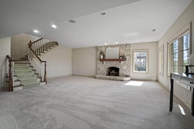 unfurnished living room with recessed lighting, carpet floors, a stone fireplace, baseboards, and stairs