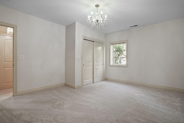 unfurnished bedroom featuring visible vents, baseboards, a closet, a notable chandelier, and light colored carpet