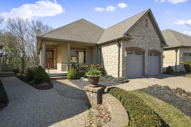 french country inspired facade with a chimney, a shingled roof, a garage, stone siding, and decorative driveway