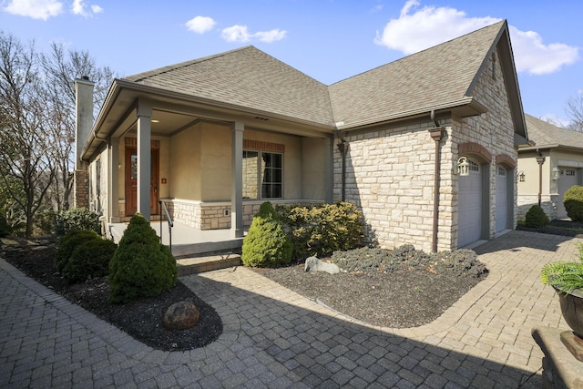 exterior space with covered porch, a chimney, a shingled roof, a garage, and stone siding