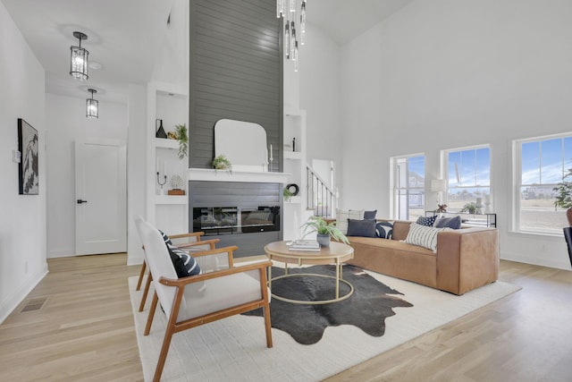 living area featuring a glass covered fireplace, a towering ceiling, visible vents, and wood finished floors