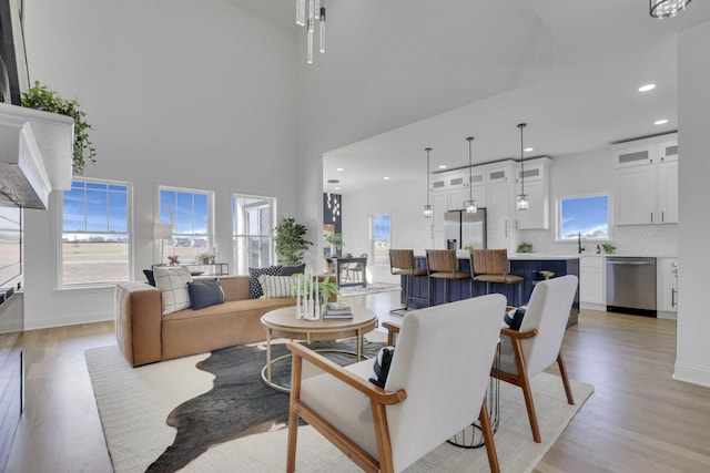 living area with recessed lighting, baseboards, a towering ceiling, and light wood finished floors