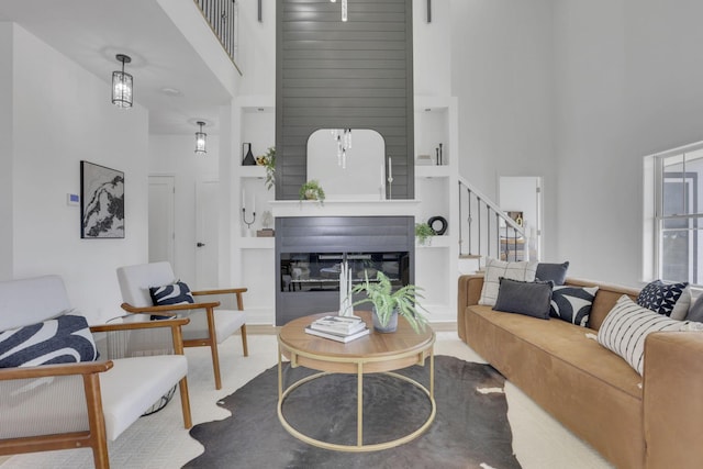 living room featuring built in features, a high ceiling, a glass covered fireplace, and stairs