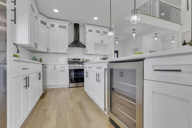 kitchen featuring light wood-type flooring, wine cooler, stainless steel stove, wall chimney exhaust hood, and light countertops