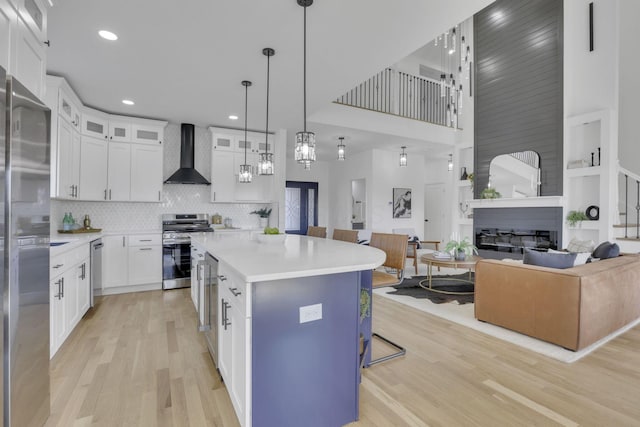 kitchen featuring light wood-style flooring, appliances with stainless steel finishes, open floor plan, and wall chimney range hood