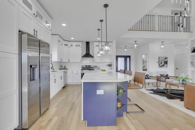 kitchen with light countertops, decorative backsplash, light wood-style flooring, stainless steel appliances, and wall chimney exhaust hood