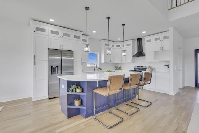 kitchen featuring a center island, light countertops, appliances with stainless steel finishes, wall chimney exhaust hood, and open shelves