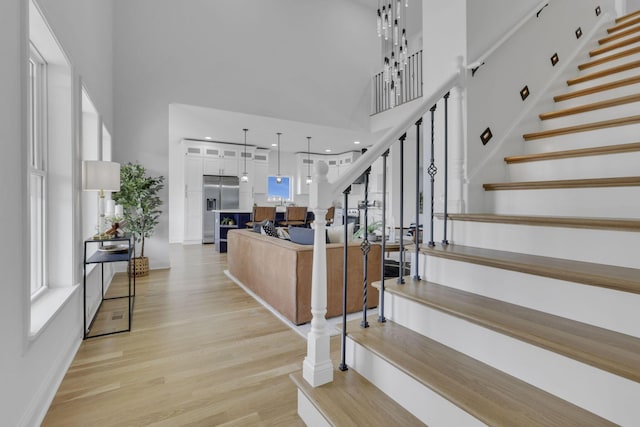 stairway featuring baseboards, a towering ceiling, and wood finished floors