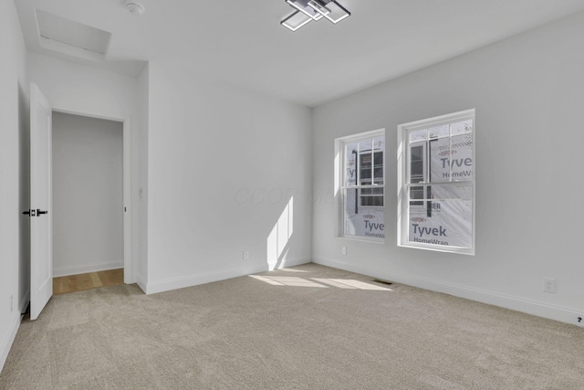 carpeted empty room featuring visible vents, baseboards, and attic access