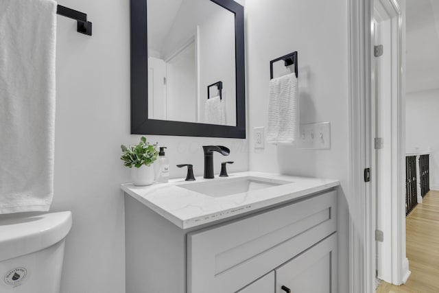 half bath featuring toilet, vanity, and wood finished floors