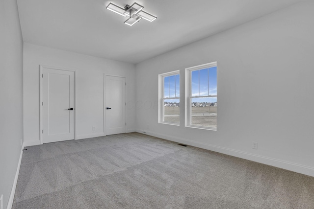 unfurnished bedroom featuring carpet flooring, baseboards, visible vents, and two closets