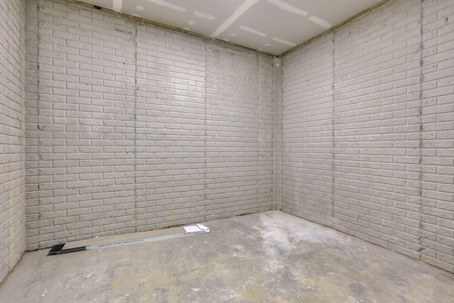 spare room featuring unfinished concrete floors and brick wall