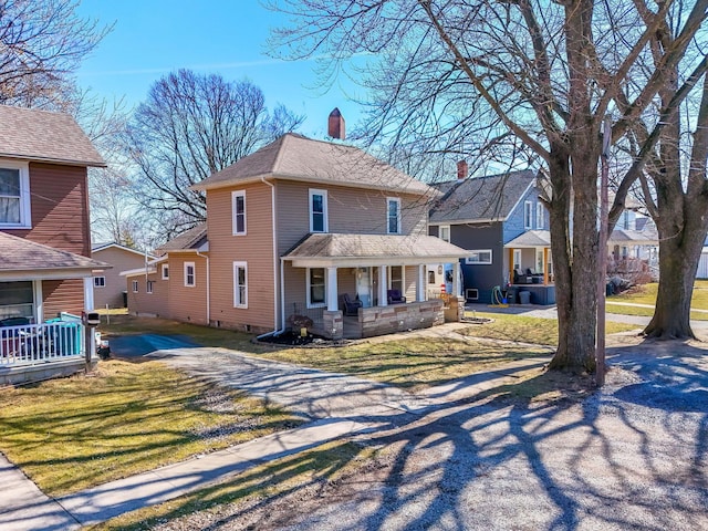 traditional style home with driveway, a front lawn, covered porch, and a chimney