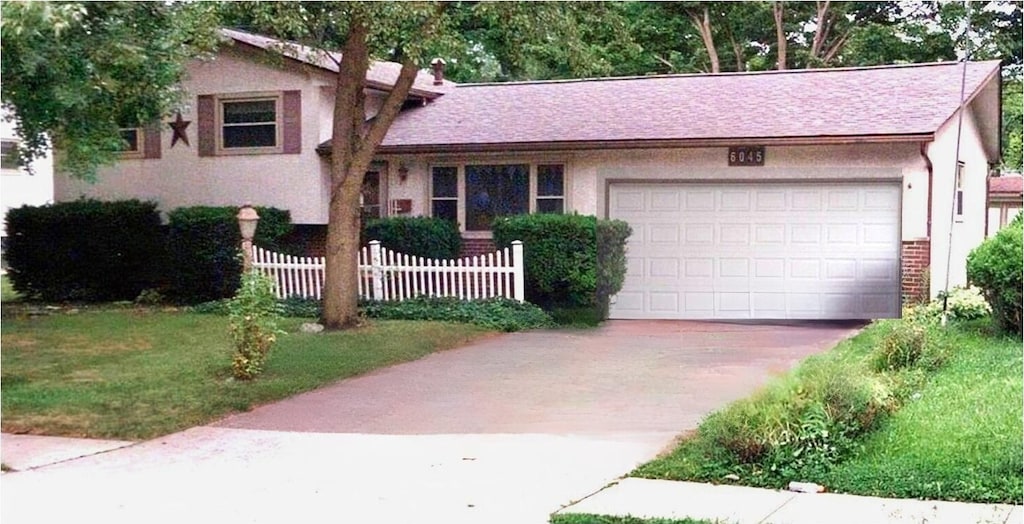 tri-level home with stucco siding, driveway, an attached garage, and fence