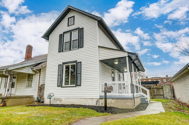 view of side of property featuring a yard, a porch, a chimney, and fence