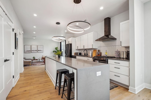 kitchen with light wood-type flooring, dark countertops, backsplash, appliances with stainless steel finishes, and wall chimney exhaust hood