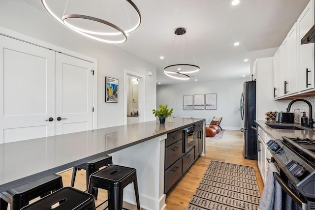 kitchen with black gas range, freestanding refrigerator, light wood-style floors, white cabinets, and a sink