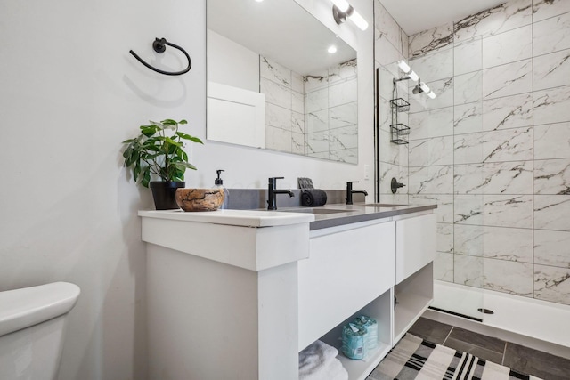 bathroom with a sink, double vanity, toilet, and tiled shower