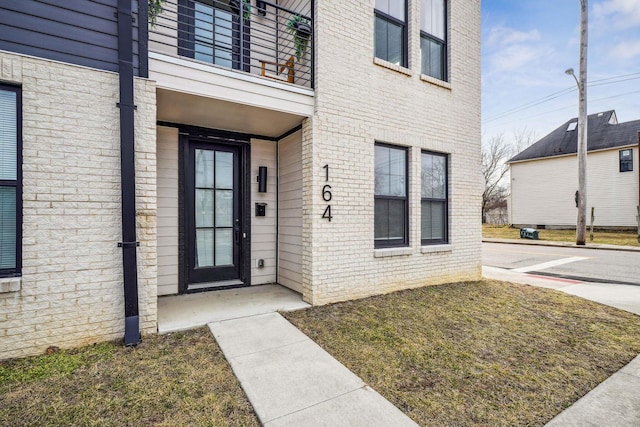 view of exterior entry with a balcony and brick siding