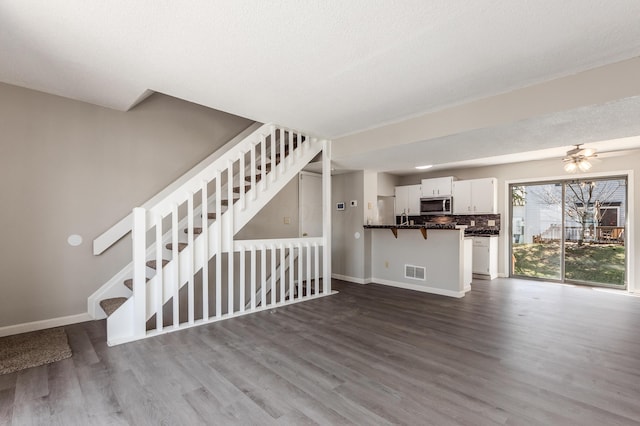 unfurnished living room featuring visible vents, stairs, baseboards, and dark wood-style flooring