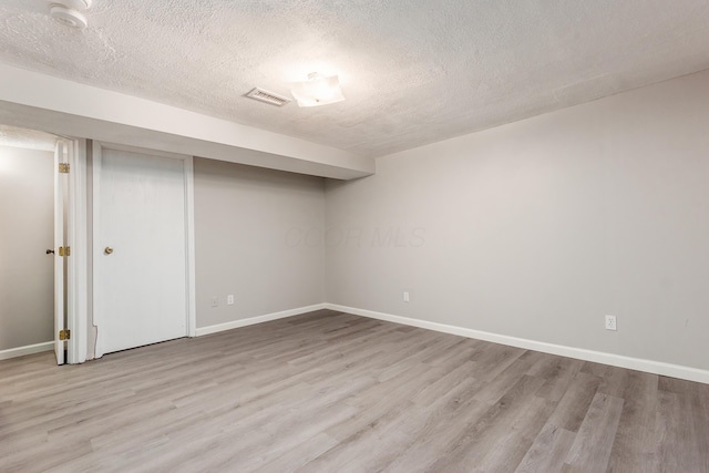 finished below grade area with visible vents, baseboards, a textured ceiling, and wood finished floors