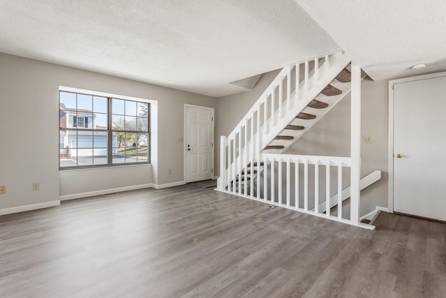 unfurnished living room with wood finished floors, baseboards, and a textured ceiling