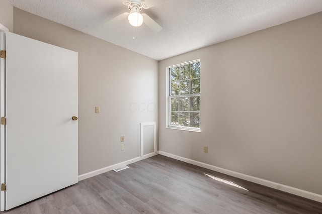 empty room featuring a ceiling fan, visible vents, wood finished floors, baseboards, and a textured ceiling