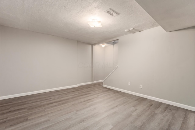 spare room with a textured ceiling, wood finished floors, visible vents, and baseboards