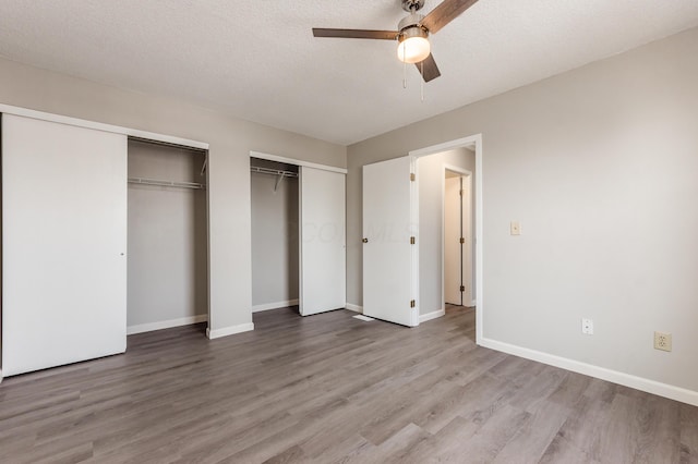 unfurnished bedroom with baseboards, a textured ceiling, multiple closets, and wood finished floors