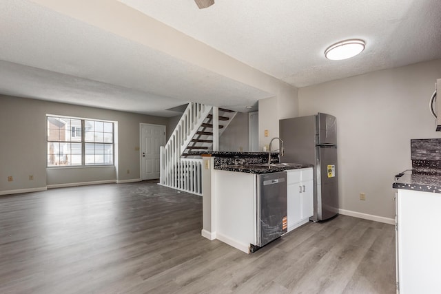 kitchen with wood finished floors, white cabinetry, a peninsula, freestanding refrigerator, and stainless steel dishwasher