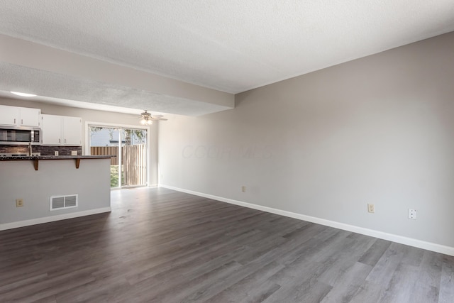 unfurnished living room with visible vents, baseboards, ceiling fan, and dark wood-style flooring