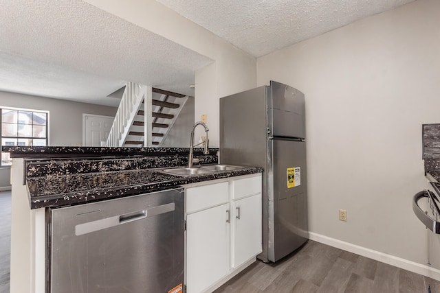 kitchen with a sink, dark wood-style floors, appliances with stainless steel finishes, white cabinets, and baseboards