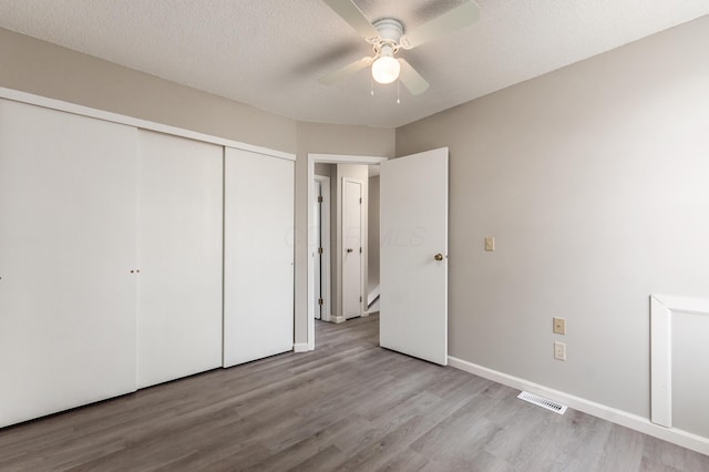 unfurnished bedroom with visible vents, a textured ceiling, wood finished floors, a closet, and baseboards