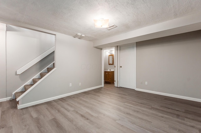 finished below grade area featuring visible vents, wood finished floors, baseboards, and a textured ceiling