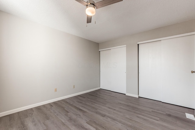 unfurnished bedroom with two closets, baseboards, wood finished floors, a textured ceiling, and a ceiling fan