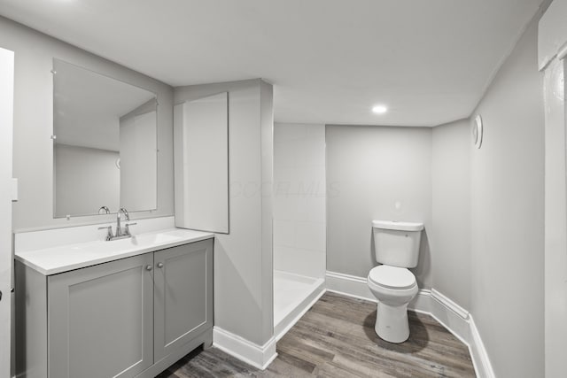 bathroom featuring vanity, wood finished floors, baseboards, tiled shower, and toilet