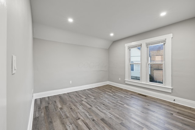 empty room featuring visible vents, wood finished floors, recessed lighting, baseboards, and lofted ceiling