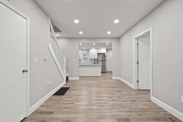 unfurnished living room featuring visible vents, light wood-style flooring, and stairway