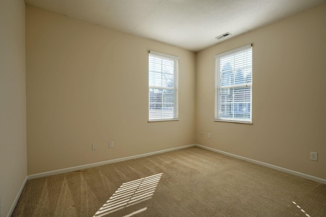 carpeted empty room featuring visible vents, a textured ceiling, and baseboards