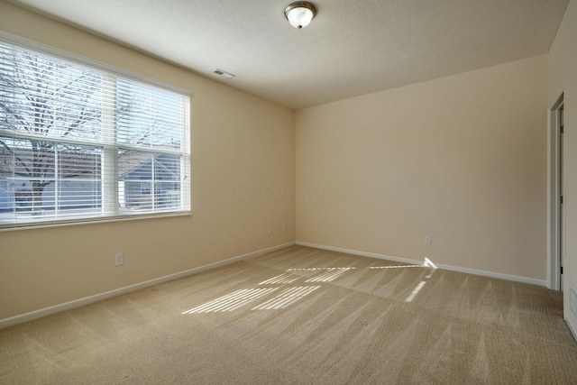 spare room featuring baseboards, light colored carpet, visible vents, and a textured ceiling