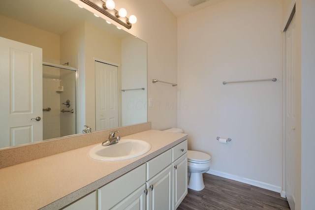 full bath with toilet, wood finished floors, a tile shower, baseboards, and vanity