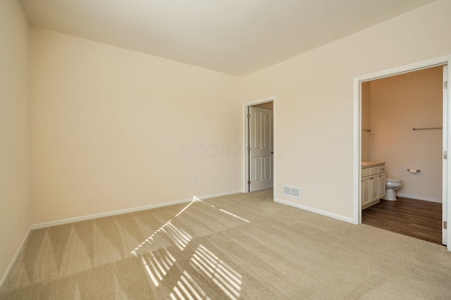 unfurnished bedroom featuring visible vents, baseboards, light colored carpet, and ensuite bathroom