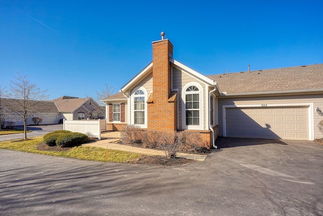 view of property exterior featuring fence, driveway, an attached garage, a chimney, and brick siding