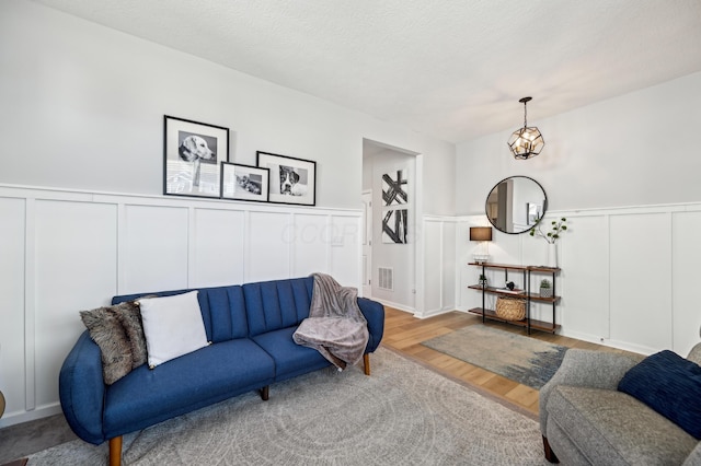 living room featuring visible vents, a textured ceiling, a decorative wall, and wood finished floors